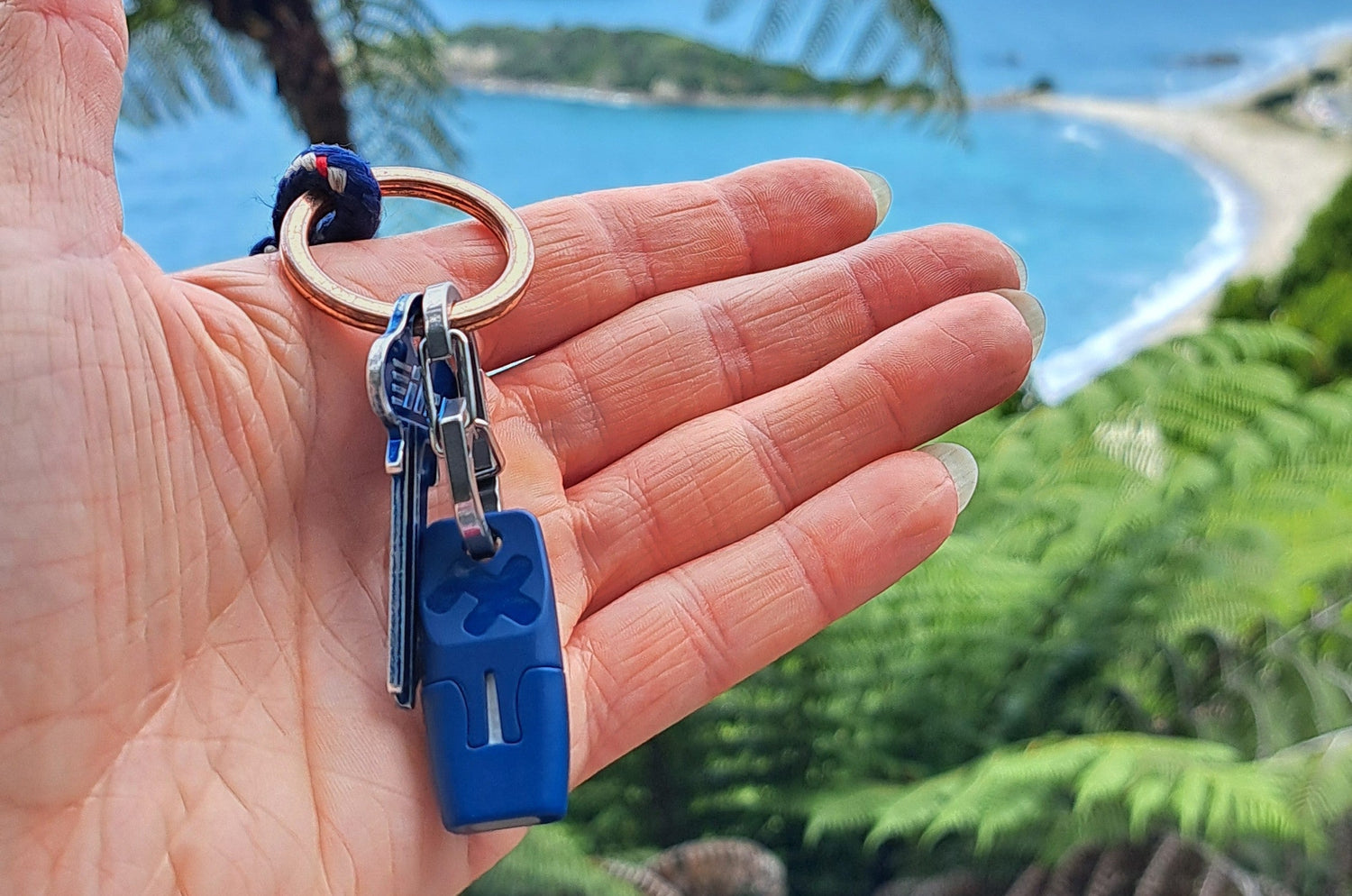 Hand holding heat it device and keys at Mount Maunganui with Moturiki Island and beach in background